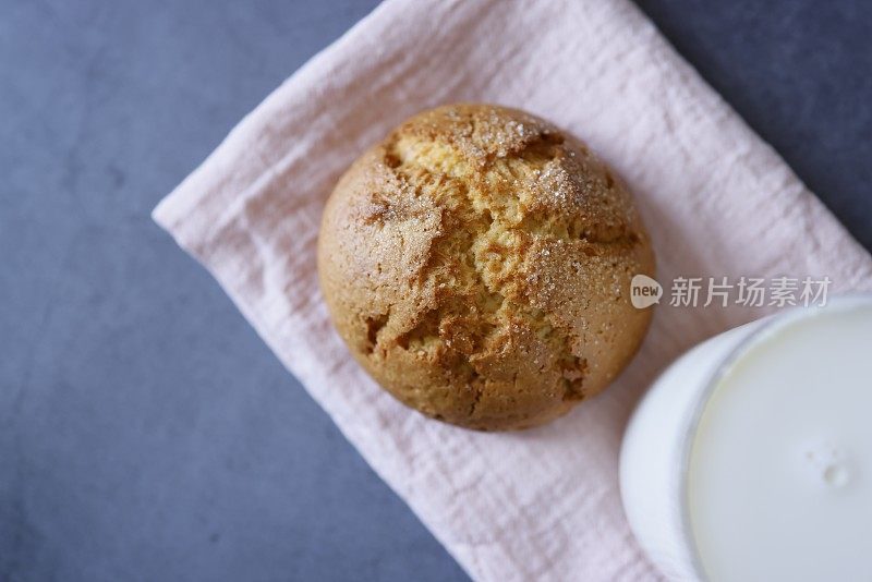 一个大的圆形橙色饼干和一杯牛奶在粉红色的亚麻布餐巾上，在一个深灰色的石头背景，特写