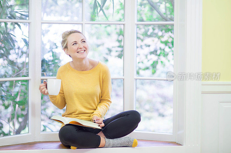 年轻貌美的白人女子坐在窗边看书喝茶