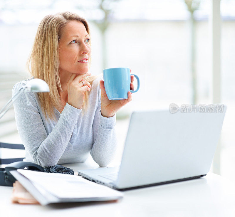 一个拿着笔记本电脑一边喝着咖啡一边看文案的成熟女人