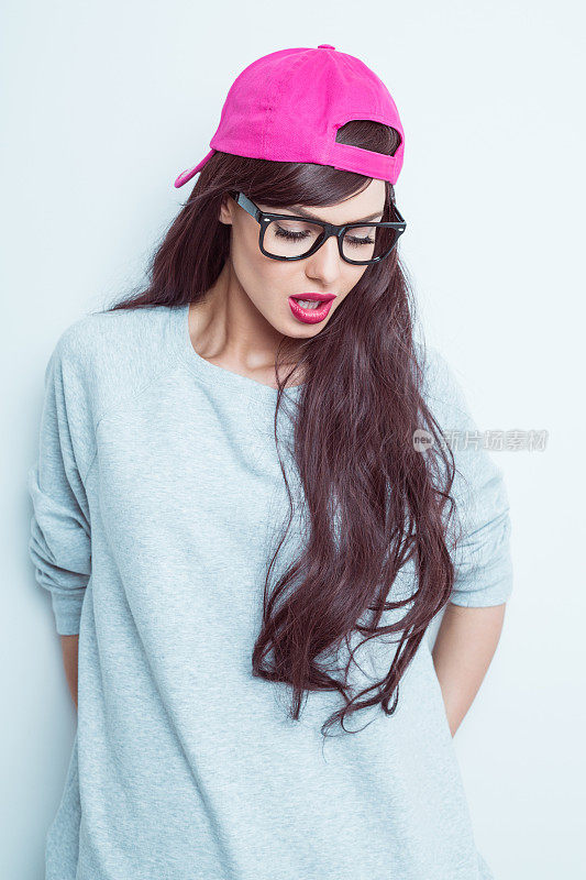 性感的年轻女人戴着书呆子眼镜和粉色棒球帽