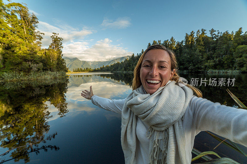 年轻女子在湖边自拍，倒影在水面上