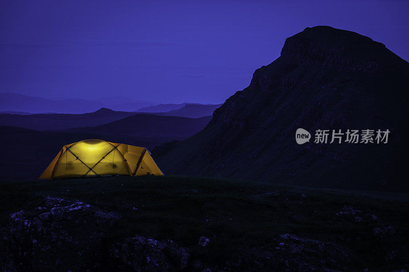 夜晚，在引人注目的山景中，被温暖的灯光照亮的圆顶帐篷