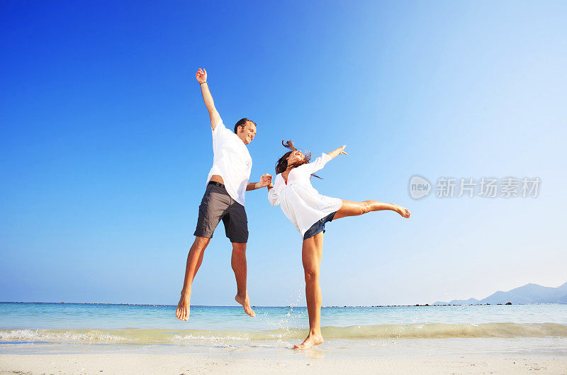 年轻夫妇在热带海滩上蹦蹦跳跳，玩得很开心。