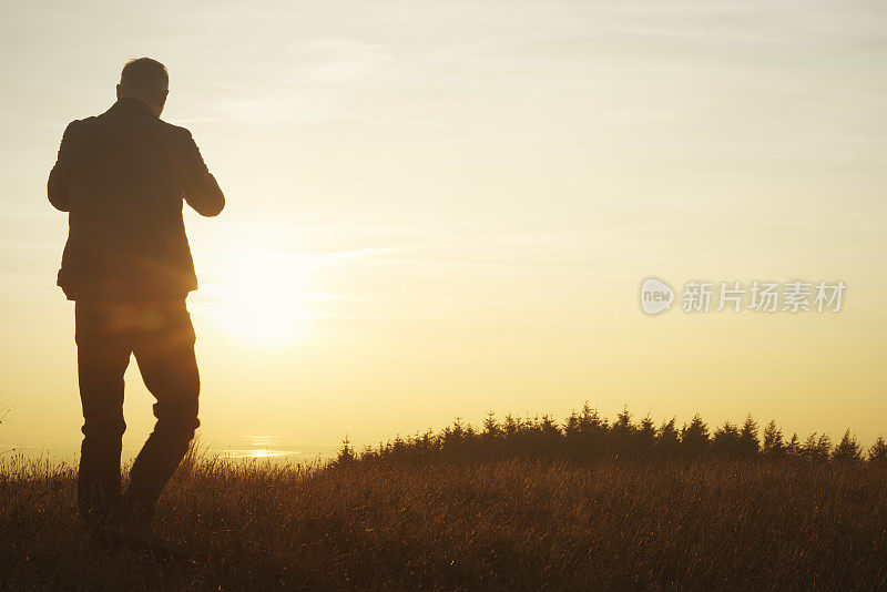 一个人站在那里用手机拍日落