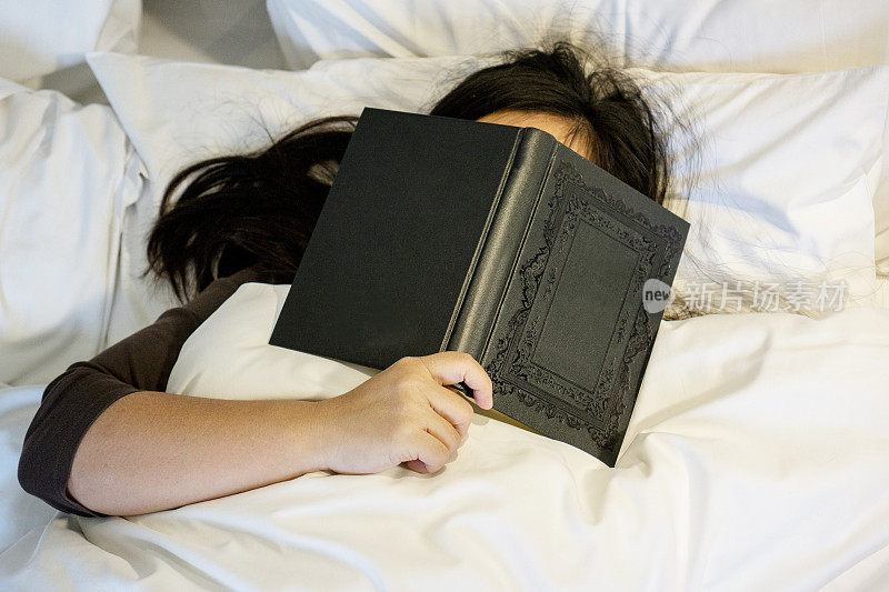 女孩用书盖着脸在床上