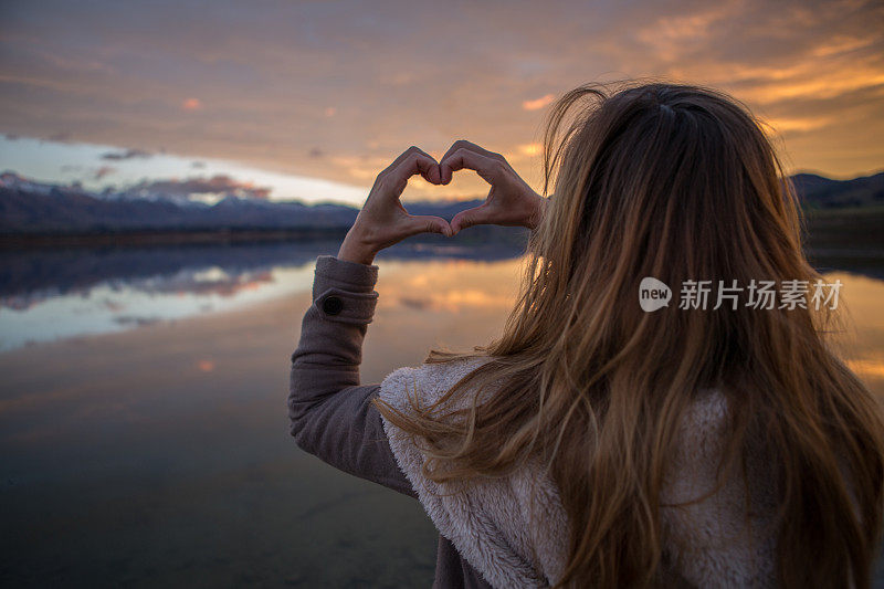 湖边的女人在火红的天空上做出心的形状