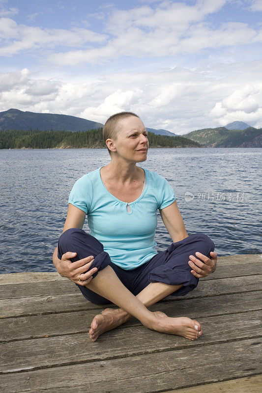 一位患乳腺癌的秃顶妇女坐在山边的码头上。