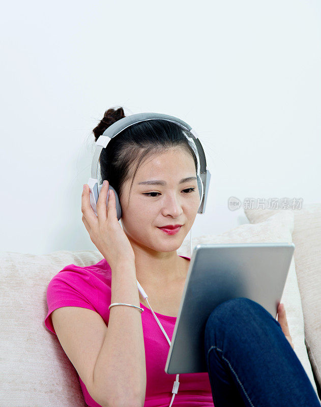 年轻女子坐在沙发上，戴着耳机和平板电脑