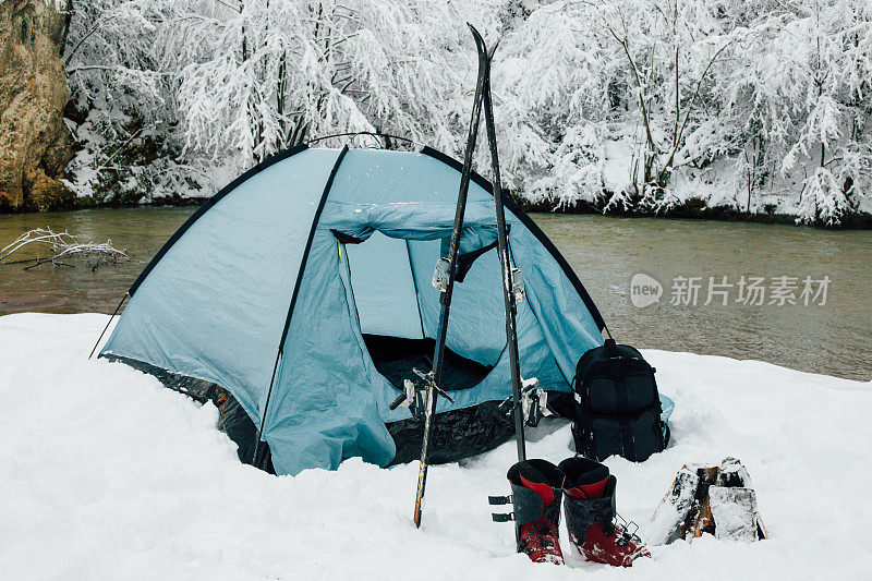 河边的露营帐篷，旁边有滑雪装备
