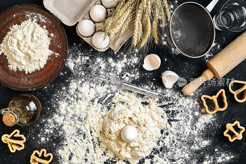 煮面团的饼干，黄油，鸡蛋，烹饪设备，面粉在黑色的桌子上。顶部视图与复制空间，菜单，食谱或烹饪类的模型。烘焙的背景