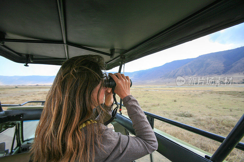 在坦桑尼亚，一名妇女在一辆游猎车的敞开式车顶上用双筒望远镜扫描恩戈罗戈罗火山口