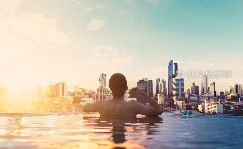 一个男人在日出的游泳池里放松，在城市的屋顶上