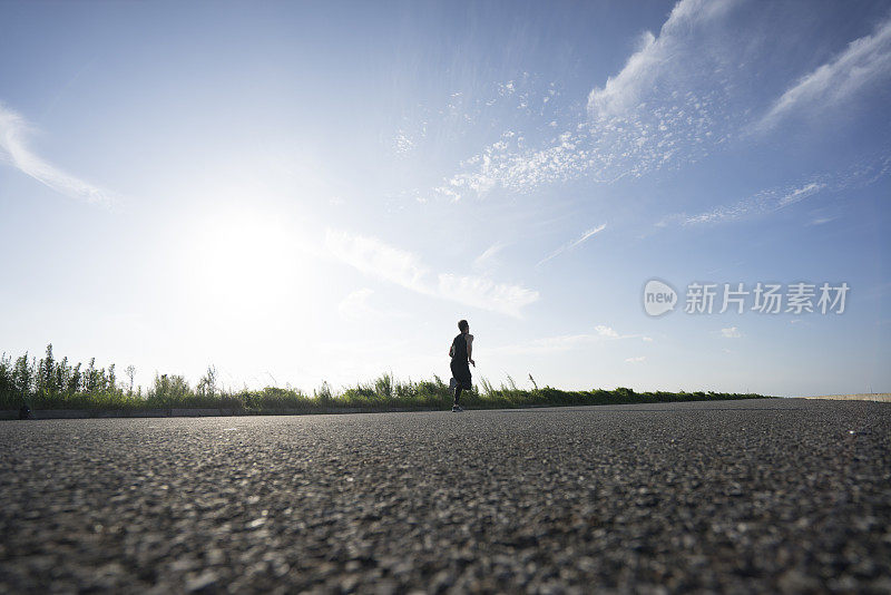 年轻的男运动员在柏油路上迎着天空奔跑