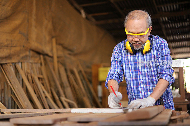 年长的亚洲木匠正在他自己的车库风格的车间里使用实心方形测量来衡量木板在退休年龄的爱好