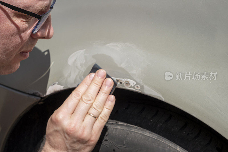 汽车油漆工，白种人，手里拿着砂纸。汽车油漆工打磨汽车机翼。