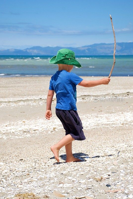 夏天在海滩上玩浮木手杖的小男孩