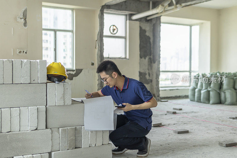 亚洲男性工程师，在装修工地处理建筑图纸和手机