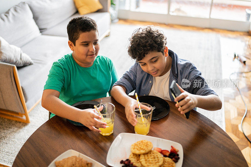 兄弟们在家里的早餐时间用智能手机进行视频通话或拍摄