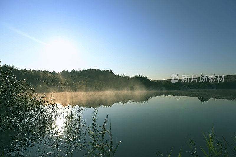 一个寒冷的夏日早晨，森林里有一个湖泊，森林的倒影和水面上的雾。雾和初升太阳的迷人风景。