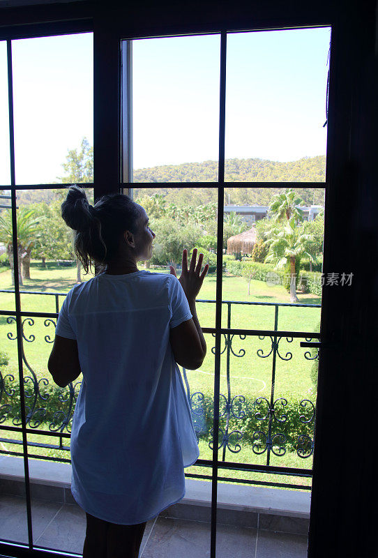 这位妇女站在那里，向窗外的全景窗眺望美丽的大花园