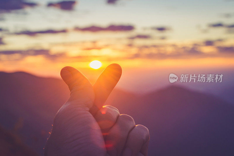 手指太阳和早晨天空的图像，两个手指在日落背景上的阴影。