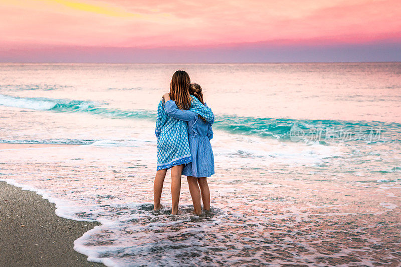 两个孩子，姐妹，在史诗般充满活力的夕阳下，一起在田园诗般的海滩上