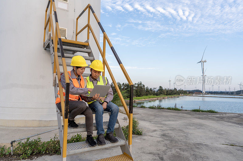 两个工程师坐在风力涡轮机的楼梯上用电脑工作