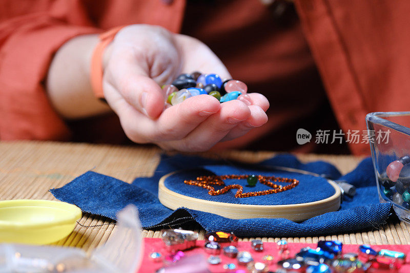 成熟女人的手坐在桌前，在家制作珠子和水晶首饰
