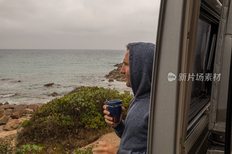 男人在他的露营车外喝茶，看海景