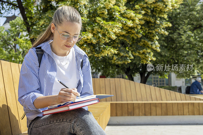 学生在户外的长凳上做笔记