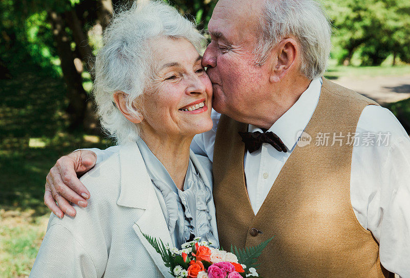 一对老夫妇在绿色的公园里散步。祖母和祖父在他们的金婚纪念日上。50年老人在一起的爱情故事。奶奶和爷爷在接吻。