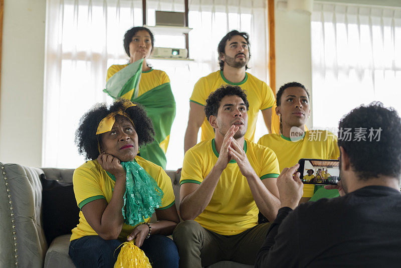 巴西队的球迷们穿着巴西队的队服和国旗在家里聚精会神地观看比赛
