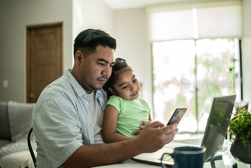父亲在家用笔记本电脑和手机和女儿一起工作