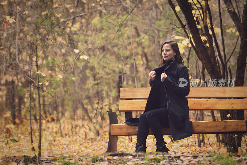 公园长凳上的年轻美女。美丽而惬意的秋天，树叶在脚下沙沙作响，抒情的秋情复制空间