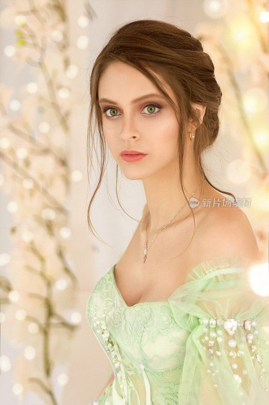 一个美丽的年轻女孩的肖像在透明的浅色连衣裙与绿色的眼睛和黑色的头发在一个精致的米色背景。一个仙女的艺术照片
