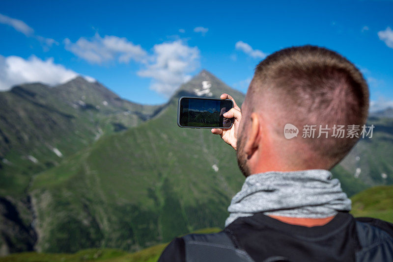 一名男子在山上用智能手机拍照的后视图