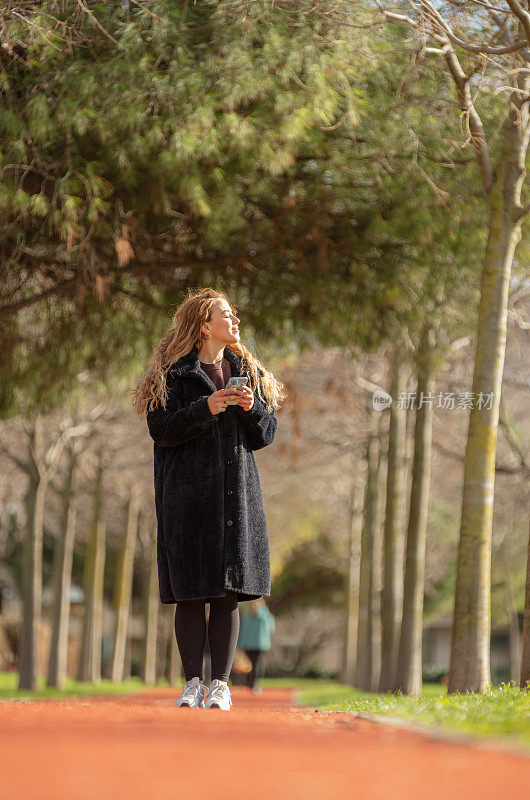 年轻女子在公园里散步。
她正在用手机发短信。