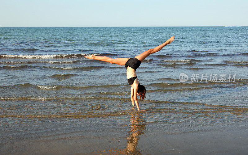 夏天，女孩在海边做体操侧手翻