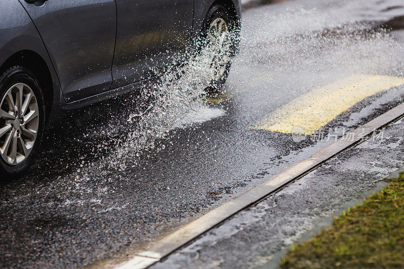 汽车驶过水坑和潮湿的柏油路。下雨了。下降。天气。水飞溅。洪水