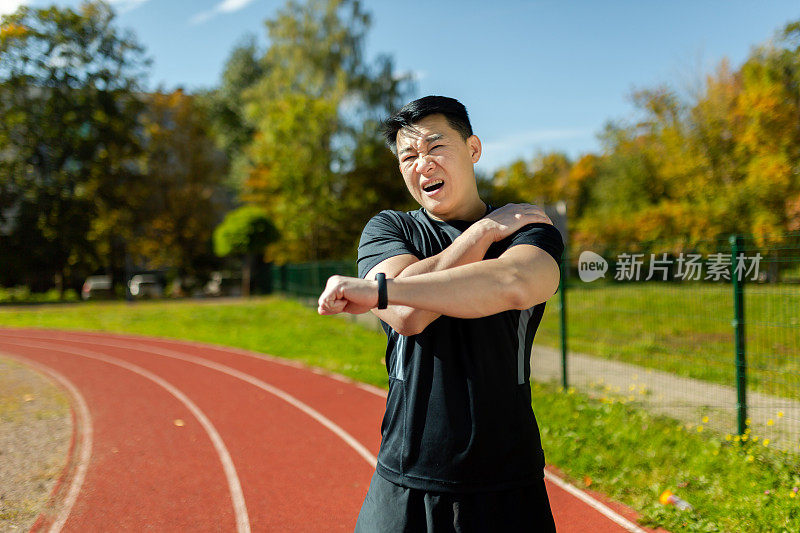 亚洲运动员伸展肩部，男子在体育场内跑步和积极的体育锻炼后伸展手臂关节，有肩部疼痛，手臂肌肉痉挛