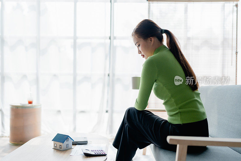 年轻女性亚洲悲伤的女士人们坐在沙发沙发在家里思考困难担心在税收费用节省问题逾期贷款延迟支付新冠病毒影响生活感到悲伤沉思住房债务的概念。
