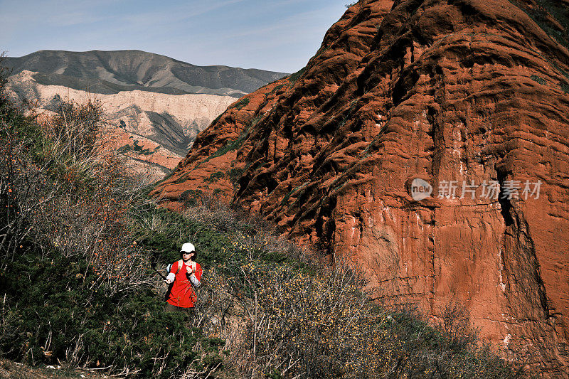 一位成熟的女游客正在红色的岩石山脉徒步旅行，并用运动相机记录下了这一过程