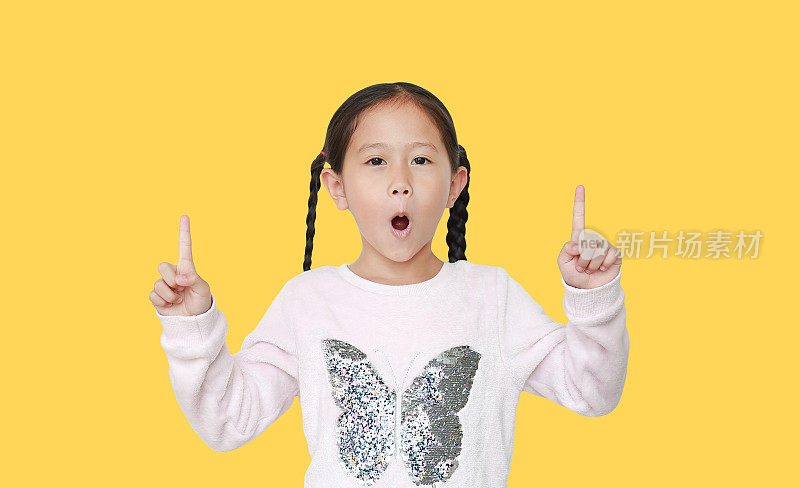 兴奋的小女孩指着两个食指孤立在黄色背景。