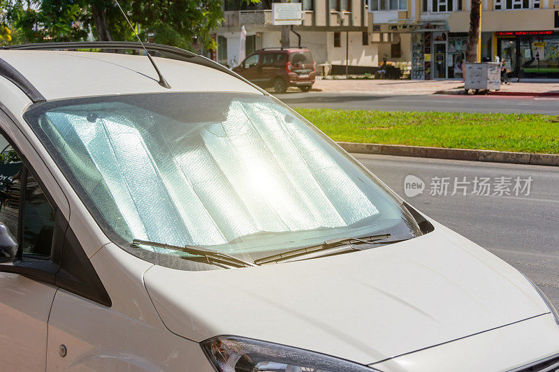 在炎热的日子里，白色轿车停在挡风玻璃下的保护性反射表面，被车内的阳光加热。