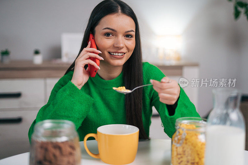 一位年轻女子正在厨房里一边吃早餐一边打电话