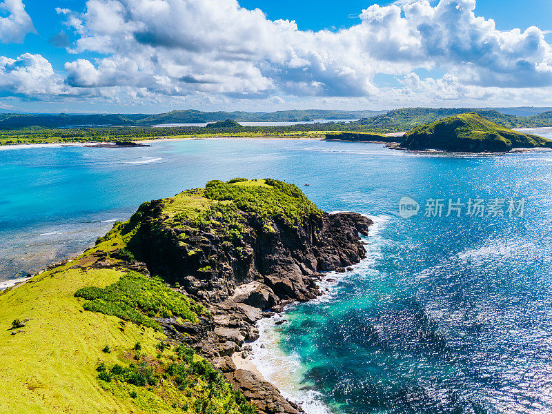 海岸景观:龙目岛，生机勃勃的绿色山坡，清澈的蓝色海水，明亮的天空和蓬松的云下的沙滩海岸线。