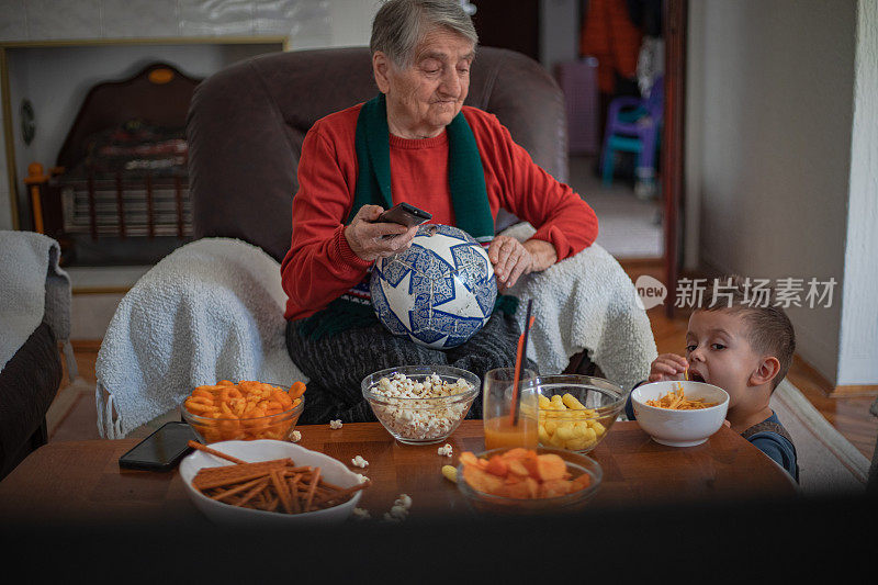 一位祖母正在家里和她的孙子一起看电视上的足球比赛