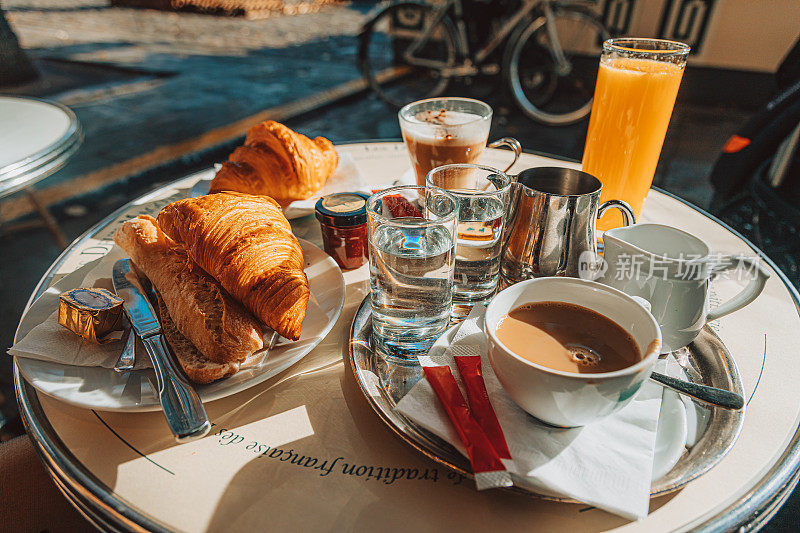 巴黎早晨的快乐:法国巴黎圣日耳曼街咖啡馆在阳光明媚的日子里的早餐场景