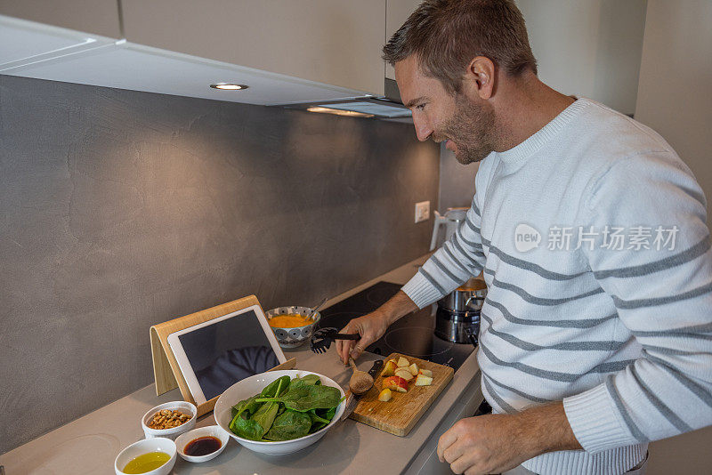 男子在厨房准备健康沙拉，跟随数码平板电脑的教程