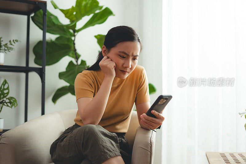 亚洲女性坐在家里看智能手机屏幕，有问题。